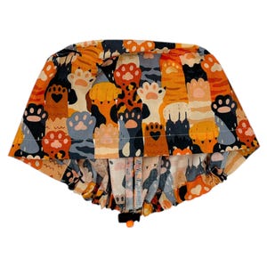 May include: A colorful surgical scrub hat with a paw print pattern in shades of orange, brown, gray, and black. The hat has a gathered elastic band at the bottom.