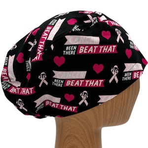 May include: Black scrub hat with a pink ribbon and the text "Beat That" repeated throughout. The hat also has the text "Been There" and pink hearts.