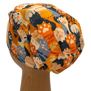 May include: Orange, gray, and black patterned scrub hat with a cat paw print design.