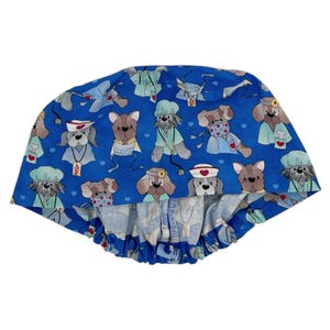 May include: Blue scrub hat with a pattern of dogs wearing medical scrubs and masks. The dogs are wearing stethoscopes, surgical caps, and holding medical tools. The hat has a blue elastic band.