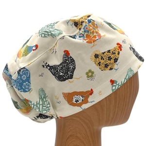 May include: A cream-coloured surgical scrub cap with a repeating pattern of colourful chickens. The chickens are depicted in various colours and patterns, including black, brown, blue, and yellow, with red combs and wattles. The cap is made of a soft fabric.