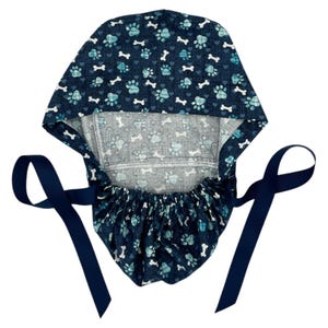 May include: A blue surgical scrub hat with a paw print and bone pattern. The hat has two long navy blue ties.