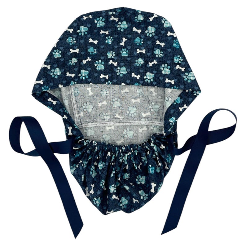 May include: A blue surgical scrub hat with a paw print and bone pattern. The hat has two long navy blue ties.