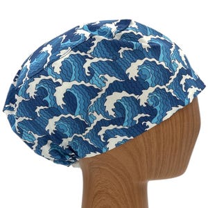 May include: A blue and white patterned scrub cap with a wave design. The cap is made of fabric and is designed to cover the head. The wave pattern is in shades of blue and white, creating a nautical theme.