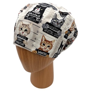 Puede incluir: Un gorro quir&uacute;rgico blanco con un patr&oacute;n repetido de fotos policiales de gatos con la palabra "WANTED" en letreros. Los gatos est&aacute;n representados en varios colores y poses, con textos como "CAT BURGLARY" y "WASTING LIVES".
