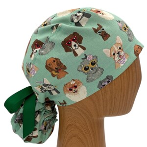 May include: A turquoise blue surgical scrub hat with a colorful dog print. The hat has a green ribbon tied at the back.