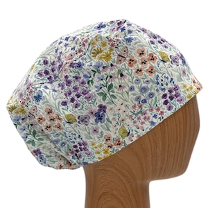 May include: A floral patterned scrub cap featuring a white background with a colorful array of flowers and butterflies in shades of purple, yellow, and blue. The cap is designed to fit comfortably and securely.
