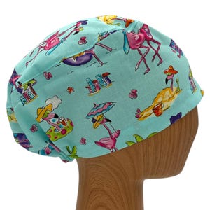 May include: A turquoise blue scrub hat with a pink flamingo and palm tree print. The hat has a white elastic band.