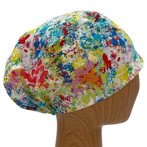 May include: A colorful surgical scrub hat with a white background and a splatter paint design in shades of red, yellow, blue, green, and pink.