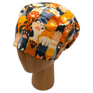 May include: A colorful scrub hat with a pattern of orange, white, and gray cat paws and tails.