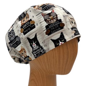 Puede incluir: Un gorro quir&uacute;rgico beige claro con un patr&oacute;n repetido de gatos de dibujos animados que sostienen letreros de "Se busca". Los letreros dicen "Peeping Tom", "Major Cattitude" y "Cat Burglar".