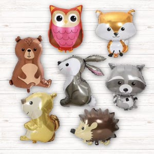 May include: A set of seven foil balloons featuring woodland animals. The balloons are shaped like an owl, fox, bear, rabbit, raccoon, squirrel, and hedgehog. The balloons are all different colors, including brown, orange, gray, pink, and gold.