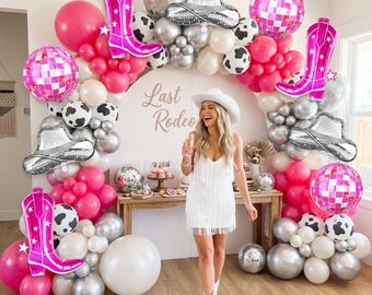 May include: A balloon arch featuring pink, white, silver, and cow-print balloons, accented with foil balloons shaped like pink cowboy boots, silver cowboy hats, and pink disco balls. A sign reads Last Rodeo in the center of the display.
