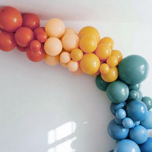 May include: A garland of balloons in shades of orange, yellow, blue, and green. The balloons are arranged in a rainbow pattern, with the orange balloons at the top and the blue balloons at the bottom.