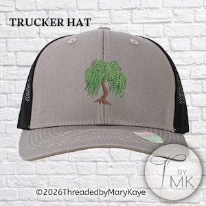 May include: A gray trucker hat with black mesh side panels and a curved brim. The front panel features an embroidered green willow tree with a brown trunk. The text TRUCKER HAT is printed at the top, and 2026ThreadedbyMaryKaye is at the bottom.