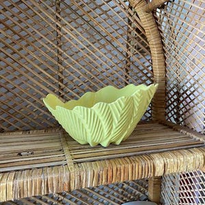 May include: A yellow ceramic bowl with a leaf design sits on a woven wicker shelf.