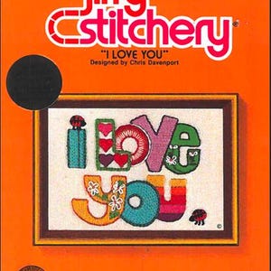 May include: A Jiffy Stitchery kit with the words "I LOVE YOU" in colorful stitched letters. The kit includes a printed design, yarn, needle, and mounting board. The background is orange.