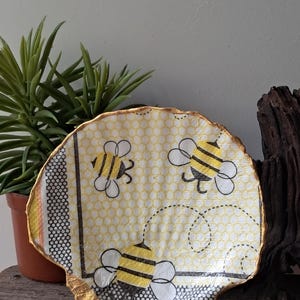 May include: A decorative seashell dish with a gold rim and a yellow and black bee pattern. The dish is decorated with a honeycomb pattern and the bees are flying around the dish.