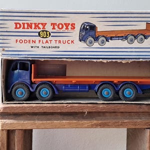 Pode incluir: Um camião plataforma Foden com plataforma traseira Dinky Toys azul e laranja, modelo 903, na sua caixa original. O camião tem rodas azuis com jantes prateadas e uma cabine azul com uma plataforma laranja.