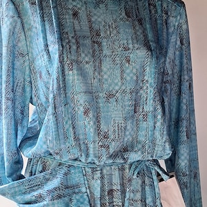 May include: A long-sleeved blue dress with a geometric pattern. The dress has a tie at the waist and a white tag attached to the sleeve.