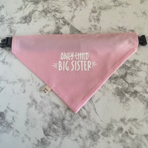 May include: Pink dog bandana with white text that reads "Only Child Big Sister".
