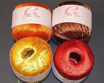 Può includere: Quattro rocchetti di filato Ella Rae Sequinicity in arancio, marrone, oro e rosso. Ogni rocchetto ha un'etichetta bianca con il nome del marchio e le parole "Sequinicity adds sparkle to any project".