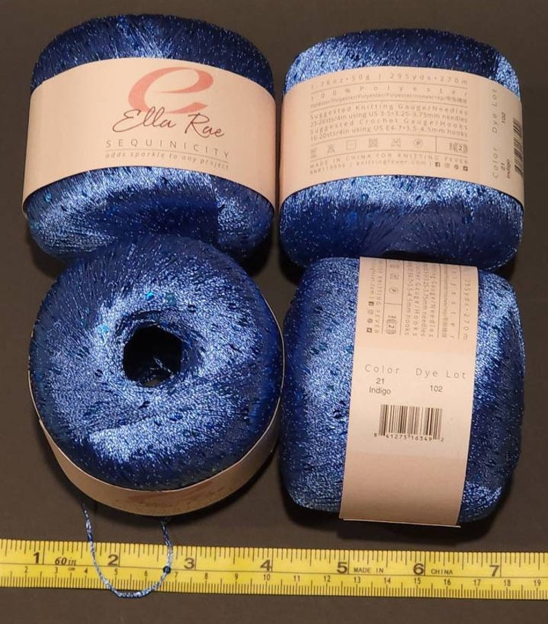 May include: Four balls of blue yarn with sequins, labelled "Ella Rae SEQUINICITY adds sparkle to any project". The yarn is 100% polyester and comes in a colour called "Indigo".