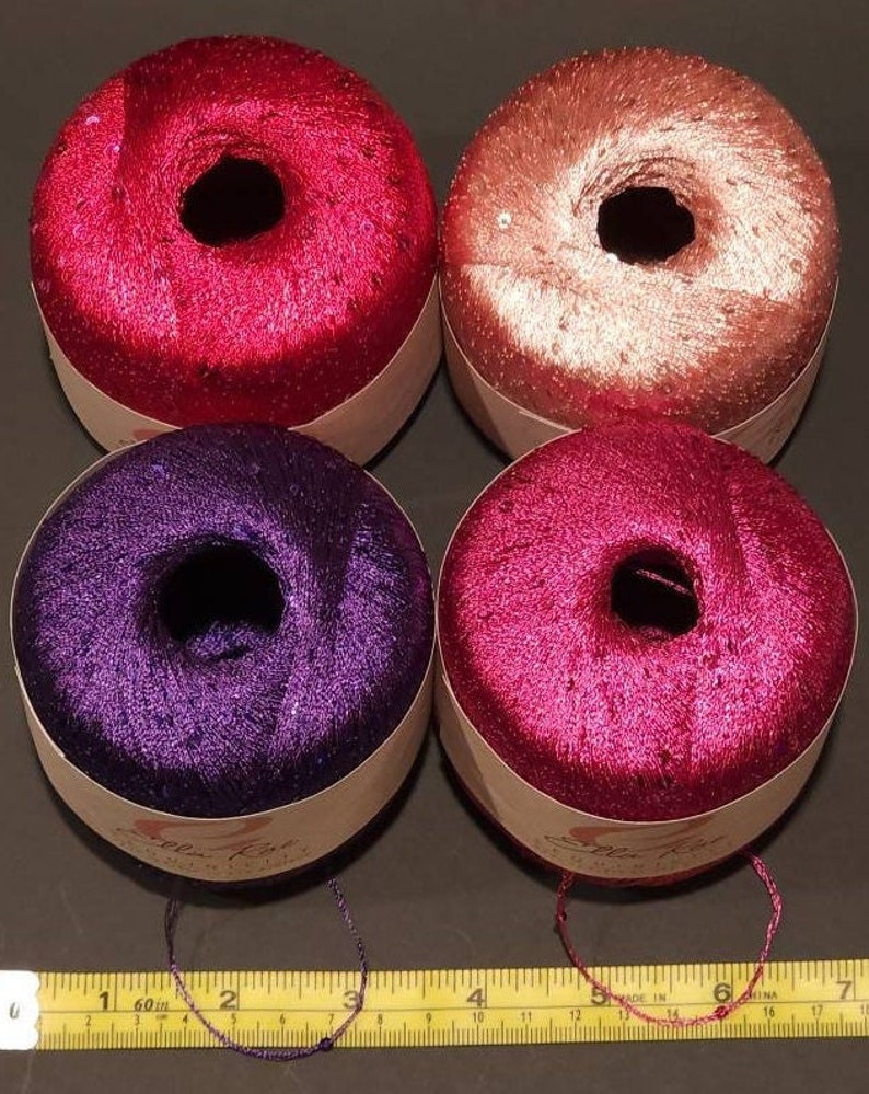 Pu&ograve; includere: Quattro rocchetti di filo in rosa, pesca, viola e rosso con una finitura scintillante. Il filo &egrave; avvolto attorno a un rocchetto di cartone con un'etichetta bianca che dice "Soleil Rose" ed &egrave; fatto in Cina.