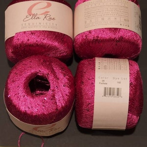 Pu&ograve; includere: Quattro rocchetti di filato rosa fucsia con paillettes. Il filato &egrave; etichettato "Ella Rue Sequinicity add sparkle to any project". L'etichetta include anche il numero di colore 26, il lotto di tintura 102 e un codice a barre.