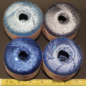 May include: Four spools of blue and silver yarn with sequins. The yarn is wound around a cardboard spool with a white label.