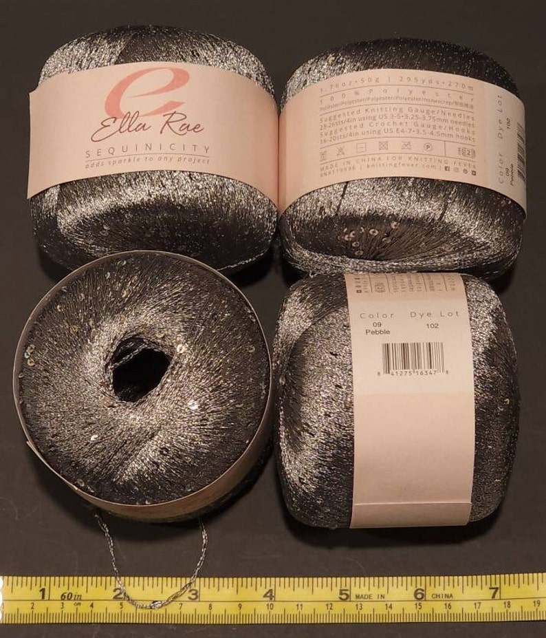 Puede incluir: Cuatro ovillos de hilo Ella Rae Sequinicity en color gris oscuro con lentejuelas plateadas. El hilo est&aacute; etiquetado con detalles que incluyen el color, el lote de tinte y el calibre de tejido sugerido. Una cadena plateada y una regla tambi&eacute;n est&aacute;n en la imagen.