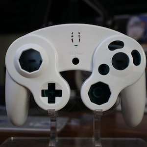 May include: White GameCube controller with a purple No Face Studio Ghibli character design on the front. The controller has a blue and white color scheme and the text "Start/Pause" is printed on the front.
