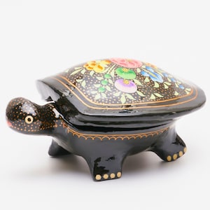 May include: A black turtle-shaped trinket box with a hinged lid. The lid is decorated with colourful floral designs on a black background. The turtle's head and feet have gold accents.