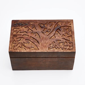 May include: A rectangular wooden box with a dark brown finish. The lid features a detailed, hand-carved relief design of a tree with spreading branches and numerous leaves. The box has a smooth, solid front panel and a hinged lid construction.