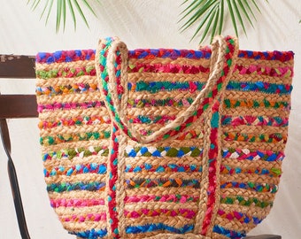May include: A large, colorful tote bag made of woven jute and fabric scraps. The bag has a striped pattern with shades of pink, blue, green, and yellow. The bag has two thick rope handles.