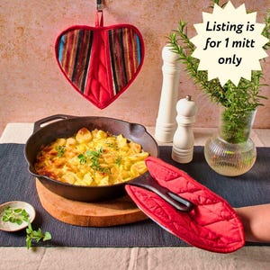 May include: A red heart-shaped oven mitt with a colorful striped design hangs above a cast iron skillet filled with a cheesy potato dish. A second red oven mitt is near the skillet. The text "Listing is for 1 mitt only" is in the image.
