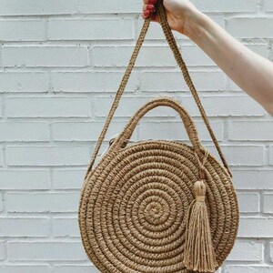 May include: A round, woven straw bag with a long strap and a tassel. The bag is brown and has a circular design.