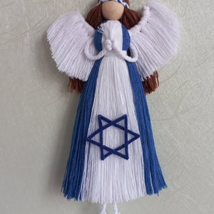 May include: A handmade angel ornament with a wooden head, brown hair, and white wings. The dress is blue and white, with a blue Star of David in the center. The angel is suspended by a brown string.