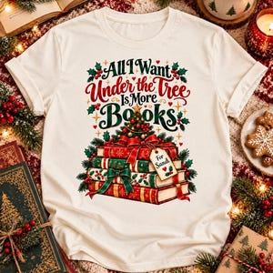 Puede incluir: Una camiseta de color crema con un gráfico de libros apilados envueltos en cintas rojas y verdes, coronados por un pequeño árbol de Navidad. El texto dice All I Want Under the Tree Is More Books, con una etiqueta de regalo que dice For Sandi.
