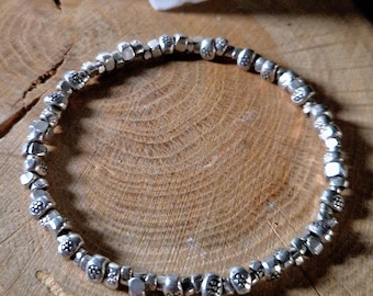 May include: A silver bracelet with small, round beads, each with a textured design. The bracelet is displayed on a wooden surface.