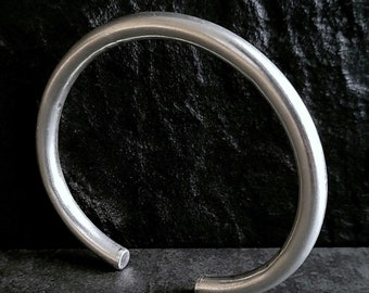 May include: A silver bangle bracelet with a smooth, rounded surface.