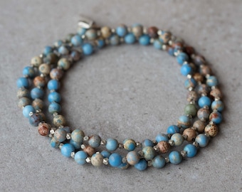 Op de afbeelding: Een drievoudige ketting gemaakt van blauwe en bruine jaspis kralen. De ketting is gemaakt van kleine, ronde kralen en heeft een zilveren sluiting.