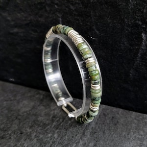May include: A silver and green beaded bracelet with a clasp closure. The bracelet is made of small, round beads that are alternating silver and green.