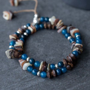 May include: A double-strand bracelet with blue, brown, and white beads. The bracelet has a sliding knot closure.