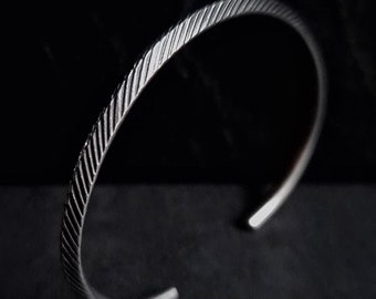 May include: A silver bangle bracelet with a textured, twisted design.