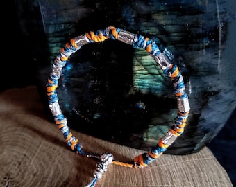 Op de afbeelding: Een blauw en oranje gevlochten armband met zilveren kralen en een zilveren kwast.