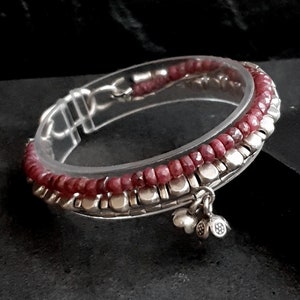 Peut inclure: Un bracelet en argent avec un charme et des perles roses. Le bracelet est composé de petites perles d'argent et de perles de pierres précieuses roses. Le charme est une fleur en argent avec un petit cœur.