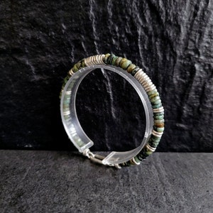 May include: A silver and green beaded bracelet with a clasp closure. The beads are small and round, and the bracelet is made of a thin, flexible material.