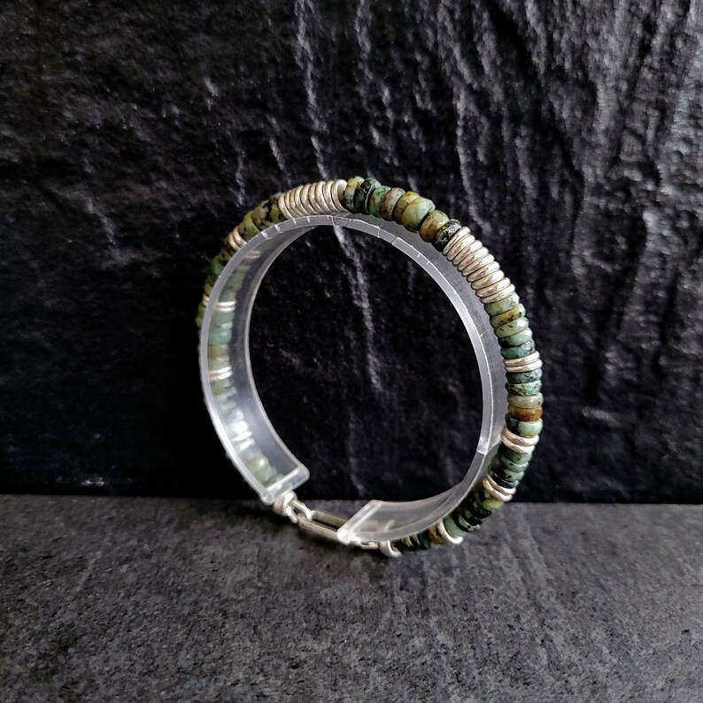May include: A silver and green beaded bracelet with a clasp closure. The beads are small and round, and the bracelet is made of a thin, flexible material.