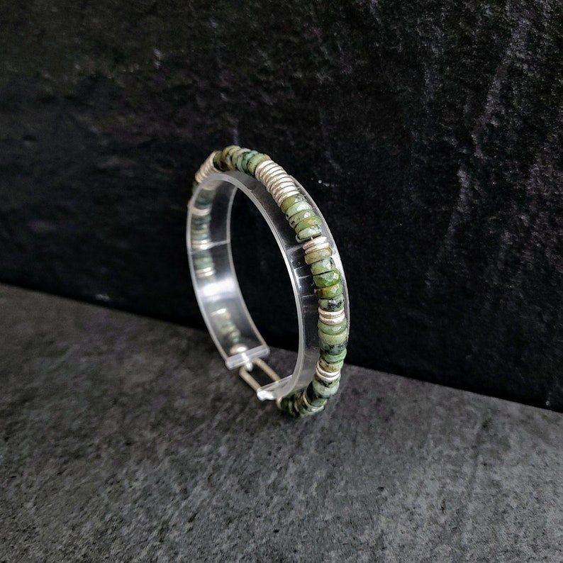 May include: A silver and green beaded bracelet with a clasp closure. The bracelet is made of small, round beads that are alternating silver and green.
